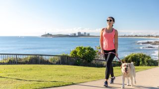The mental health benefits of walking: A woman in a pink top walks a dog near the ocean