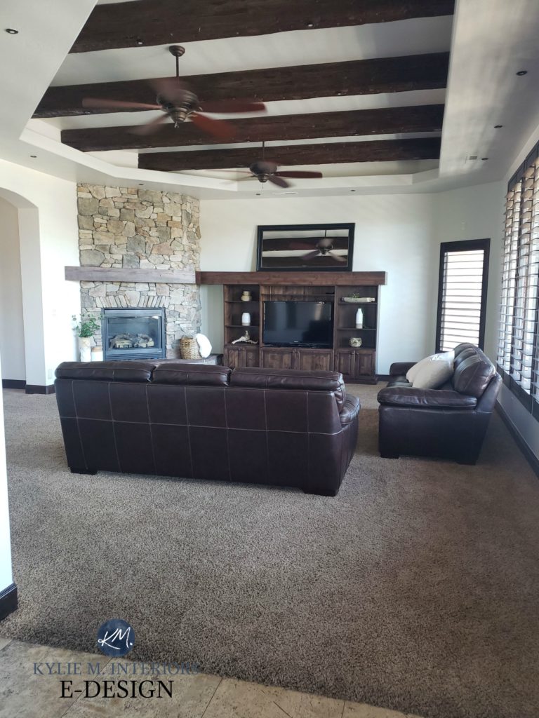 Living room with dark wood beams, trim and tv stand, stone fireplace, brown leather furniture and greige taupe 